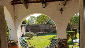 An outdoor patio with two striped chairs and a table, a potted plant, and a view of a grassy yard through an arched doorway. - Villa with garden (Castel Volturno)