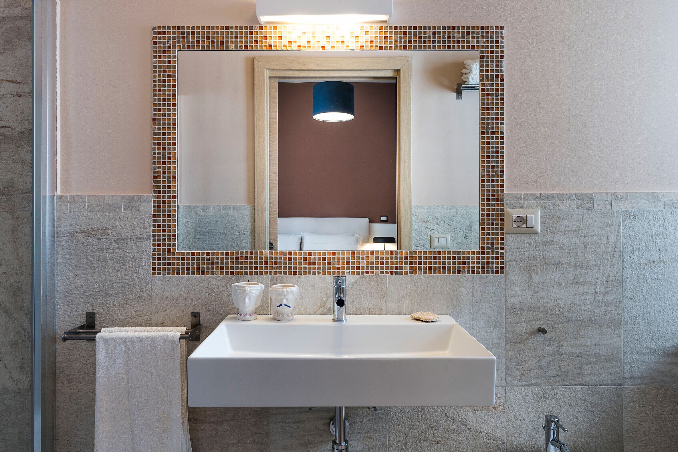 A bathroom with a white sink, a mirror with a mosaic border, and a towel hanging on a rack.