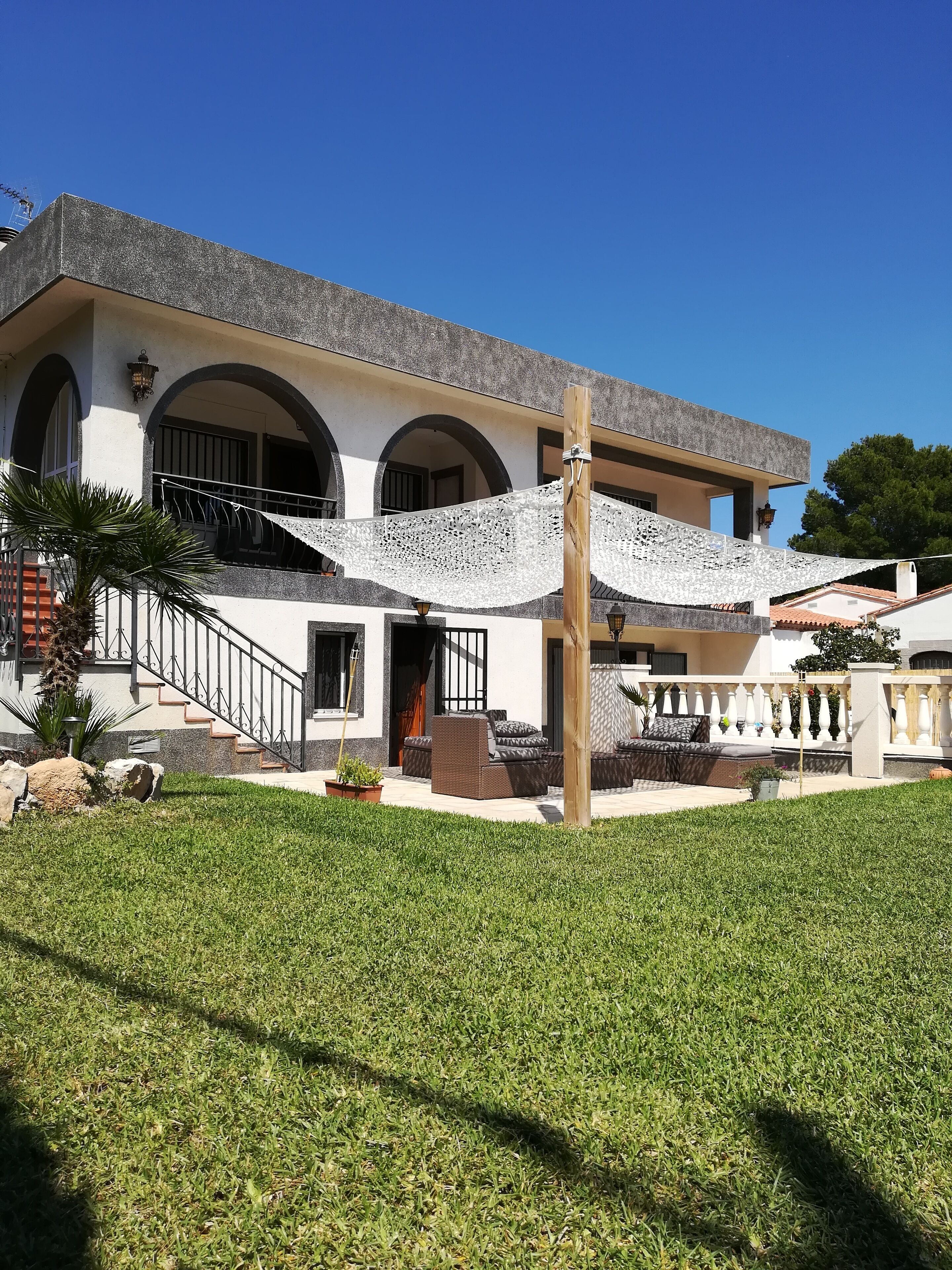 Une maison à deux étages avec un balcon, un escalier et une pelouse bien entretenue.