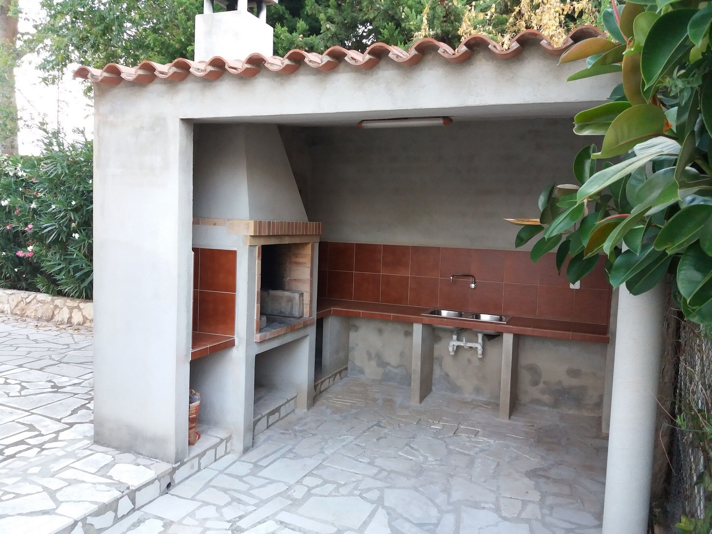 A compact outdoor kitchen with a tiled backsplash, a sink, and a built-in grill.
