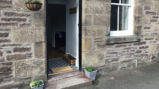 A stone building with a wooden door, a window, and a potted plant outside. - The Cottage, a romantic getaway (Dunblane)