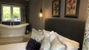 A bedroom with a large bed, a bathtub, and two framed floral paintings on the wall. - The Cottage, a romantic getaway (Dunblane)