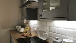 A kitchen with a black induction cooktop, a toaster, a salt and pepper set, and a wooden cutting board. - The Cottage, a romantic getaway (Dunblane)