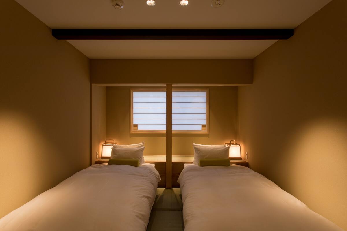 Quarto de hotel com duas camas, uma janela com persianas e abajures.