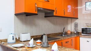Een keuken met oranje kastjes, een magnetron, een waterkoker, een broodrooster en een spoelbak.