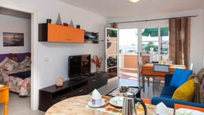 Een moderne woonkamer met een televisie, een salontafel en een eethoek met een tafel en stoelen.