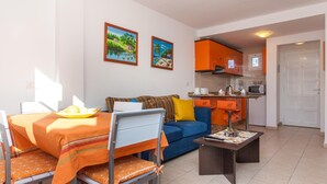 Een compacte leefruimte met een eethoek, een bank, een salontafel en een kitchenette.