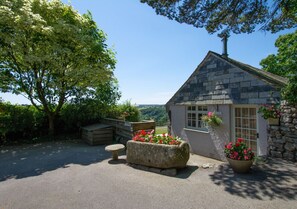 Situated in a serene setting, this charming cottage features a cozy porch with a bench and flower bed.