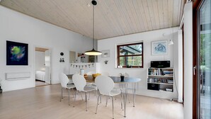 A modern kitchen with white cabinets, a dining area with a wooden table and white chairs, and a bookshelf filled with books and decorative items. - Cozy home in ålbæk with WiFi (Ålbæk)