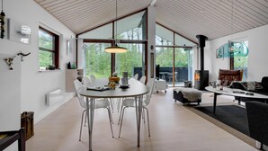 A modern interior with a dining area, a fireplace, and large windows offering a view of the outdoors. - Cozy home in ålbæk with WiFi (Ålbæk)