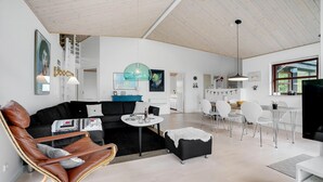 A modern living room with a black sofa, a brown leather chair, and a dining area with white chairs and a wooden table. - Cozy home in ålbæk with WiFi (Ålbæk)