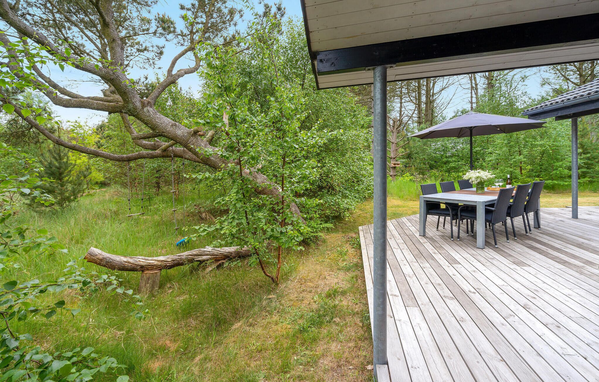 Eine Terrasse im Freien mit Tisch und Stühlen, umgeben von üppigem Grün und einem großen Baum.