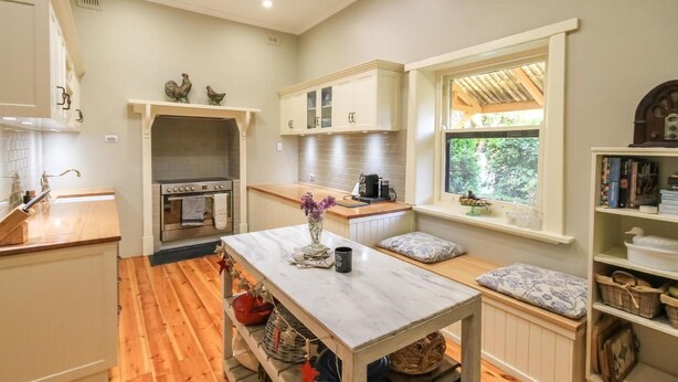 A kitchen with wooden flooring, a central island, white cabinetry, and a window with a view of greenery. - Ambrosia Holiday Home (Tanunda)