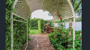 A garden pathway leading to a gazebo with a lattice roof, surrounded by lush greenery and potted plants. - Ambrosia Holiday Home (Tanunda)