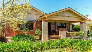 A two-story house with a brick facade, a front porch, and a well-maintained garden with various plants and a tree. - Ambrosia Holiday Home (Tanunda)