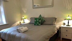 A neatly made bed with rolled towels, a green patterned pillow, and two bedside lamps. - Ambrosia Holiday Home (Tanunda)