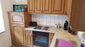 A compact kitchen with wooden cabinets, a built-in oven, a stovetop, a toaster, and a coffee maker.