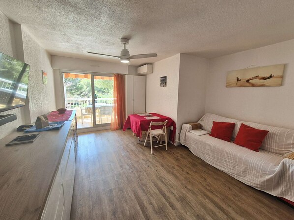 A room with a dining table, a sofa, a ceiling fan, and a sliding glass door leading to an outdoor area.