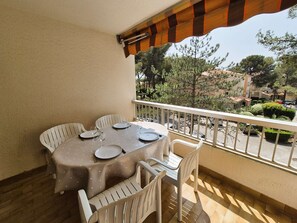 A balcony with a table set for four, white chairs, and a view of trees and buildings.