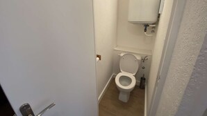 Une petite salle de bain blanche, avec des toilettes, un lavabo et un miroir.