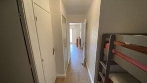 Un couloir étroit avec un plancher en bois, des murs blancs et un lit superposé sur le côté droit.