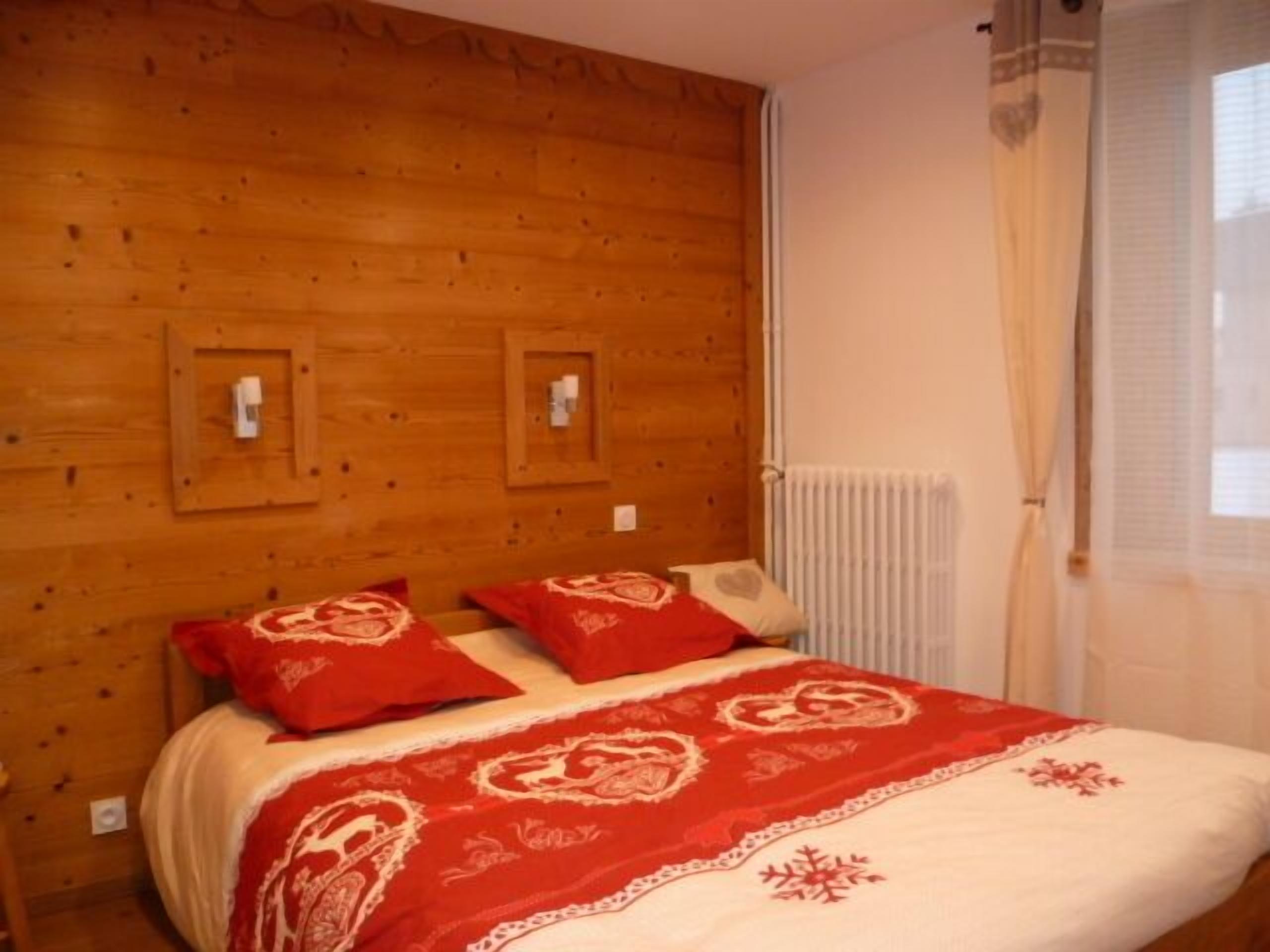 Una habitación con paneles de madera, una cama, dos interruptores de luz en la pared y una ventana con cortinas.