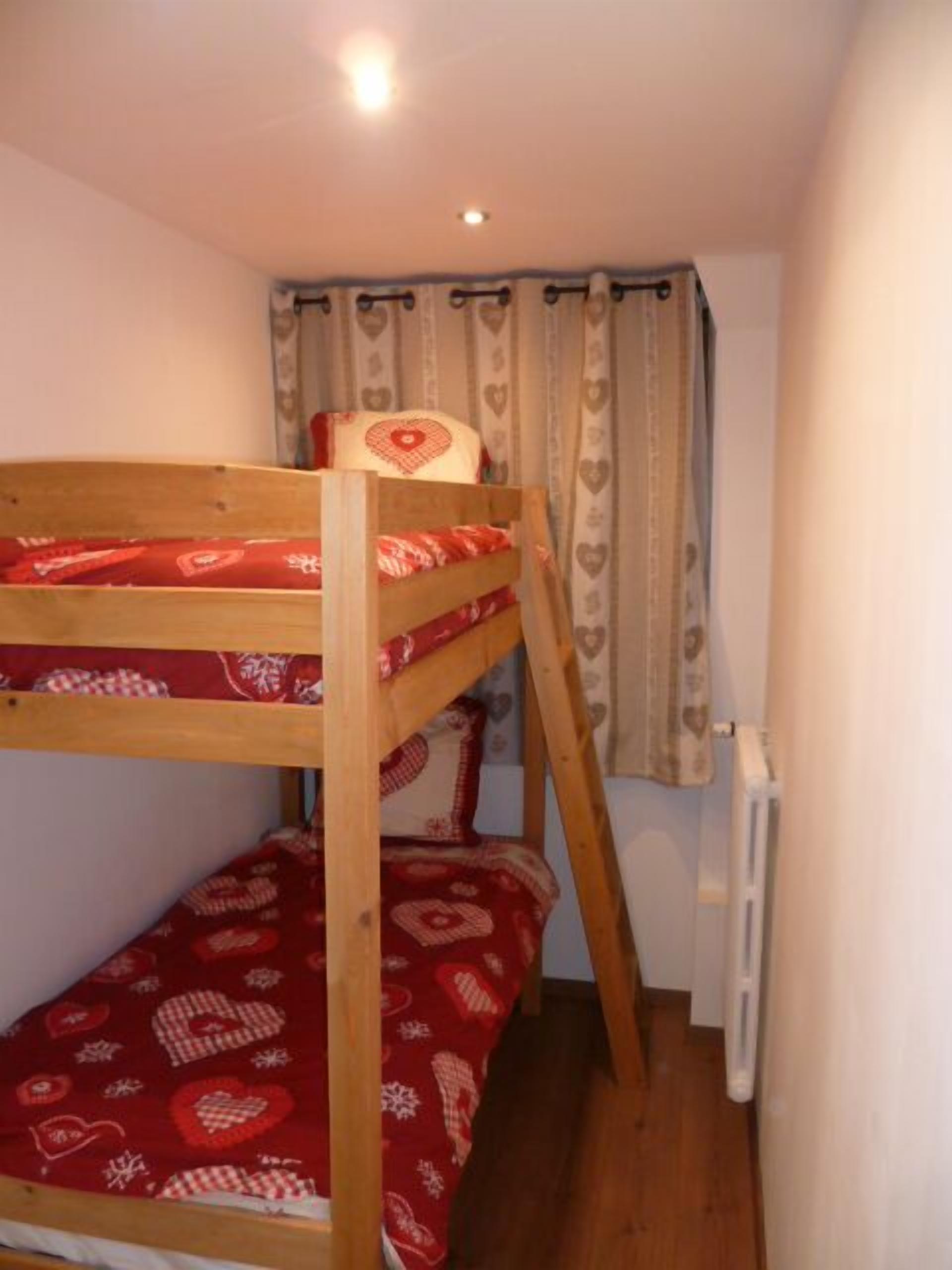Una cama litera con un edredón rojo estampado, un cabecero de madera y una ventana con cortina.