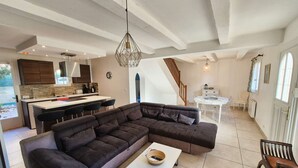 Ein modernes Wohnzimmer mit einem Ecksofa, einem Essbereich mit rundem Tisch und einer Küche mit Holdekor-Schränken und einer integrierten Kochinsel.