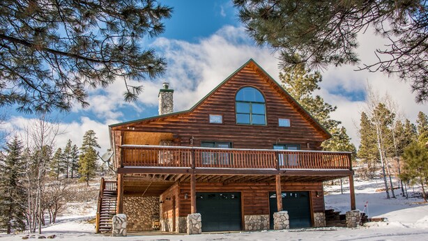 A log cabin with a balcony, stone foundation, and a large arched window.
