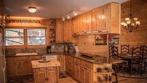 A wooden kitchen with a large window, wooden cabinets, a granite countertop, and a chandelier.