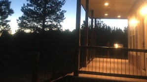 A wooden deck with a railing, a covered porch, and a view of the sky with a crescent moon.