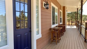 A covered porch with wooden tables and benches, a dark blue door, and a white-framed window.