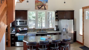 A modern kitchen with a central island, bar stools, stainless steel appliances, and large windows.