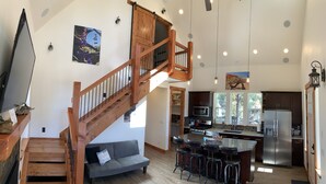 A spacious kitchen with a central island, a wooden staircase, and a grey sofa.