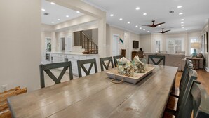 A spacious dining area with a wooden table and chairs, a kitchen in the background, and a living area with a sofa and a lamp. - Pool, 3 Mins to the Beach, Hidden Oasis in BMB + Free Attraction Tickets! (Santa Rosa Beach)