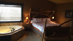 Een slaapkamer met een groot bad, een houten hoofdbord, twee bedlampen en een raam met zonwering.