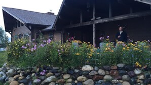 Een rustiek gebouw met een schuin dak, omgeven door een tuin met verschillende bloemen en een stenen muur.