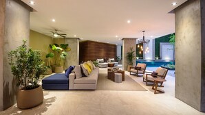 Un espace de vie moderne comprenant un canapé, des fauteuils et une table basse. On aperçoit une piscine à l’arrière-plan.