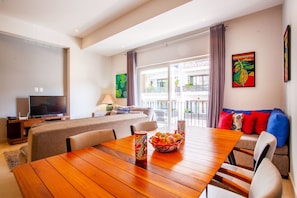 Una sala de estar moderna con una mesa de comedor de madera, un sofá, un televisor y un balcón con cortinas.