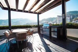 An outdoor patio with a table and chairs, a grill, and a view of a mountainous landscape. - Modern Condo @ Zenith in Zona Romantica | 2 Baths, Pool, Gym (Puerto Vallarta)