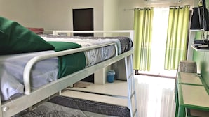 A dormitory room with bunk beds, a desk, and a chair. There is a window with curtains, a door, and a trash bin.