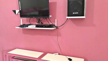 Una pared rosa con una computadora que incluye un monitor, un altavoz y un escritorio.