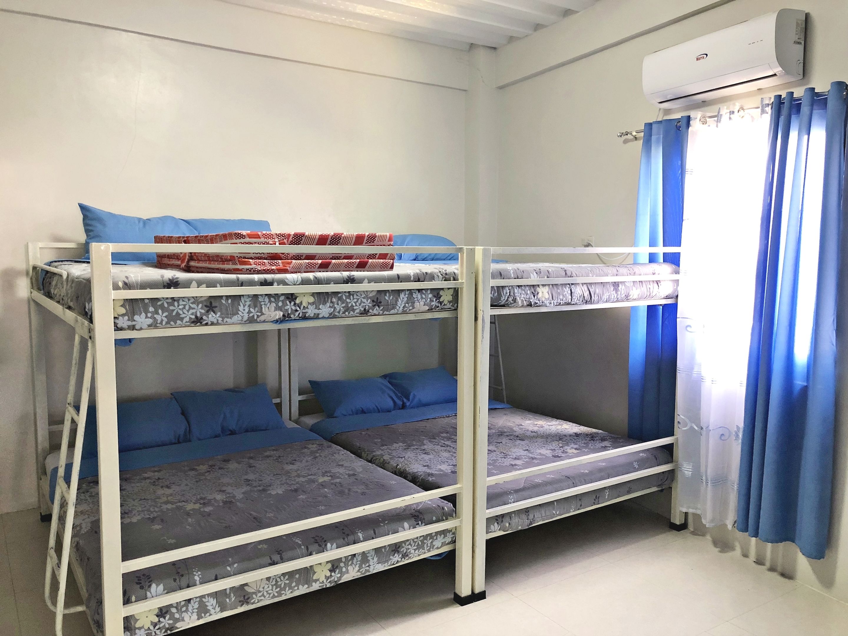 Habitación con literas, aire acondicionado blanco y cortinas azules.