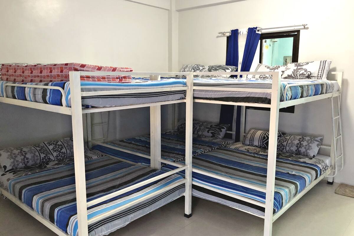 Habitación con literas, ropa de cama a rayas y una ventana con cortinas azules.