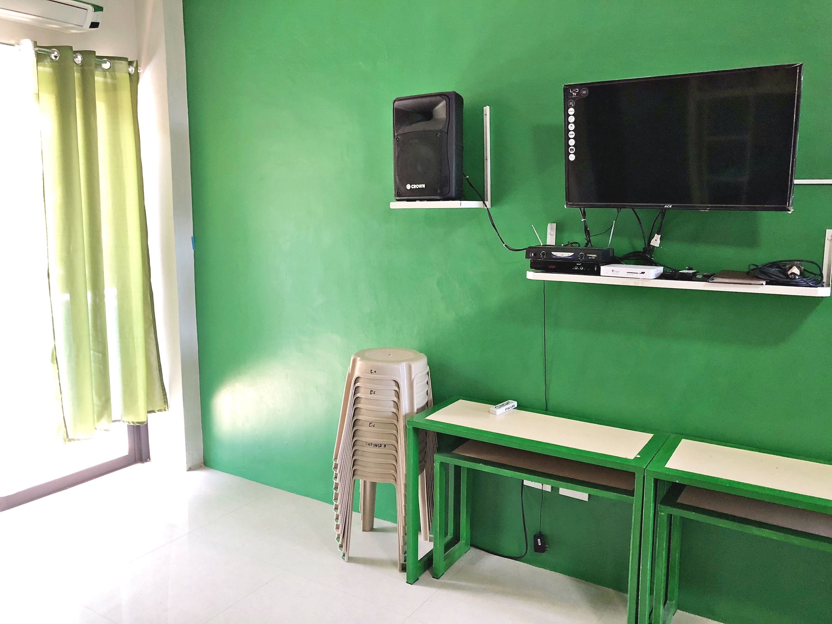 Una stanza con una parete verde, una scrivania, una sedia, un televisore e un altoparlante.