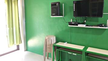 Una stanza con una parete verde, una scrivania, una sedia, un televisore e un altoparlante.