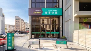 Een meerlaags hotel met een Checkinn Express bord, een groen bord en een hekpoort.