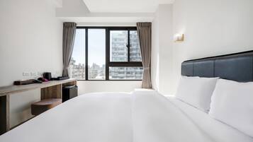 Quarto de hotel moderno com uma cama grande, uma escrivaninha de madeira e vista para a cidade através de uma janela ampla.