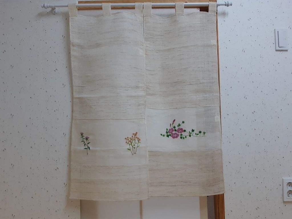 A pair of curtains with floral embroidery, hanging on a rod.
