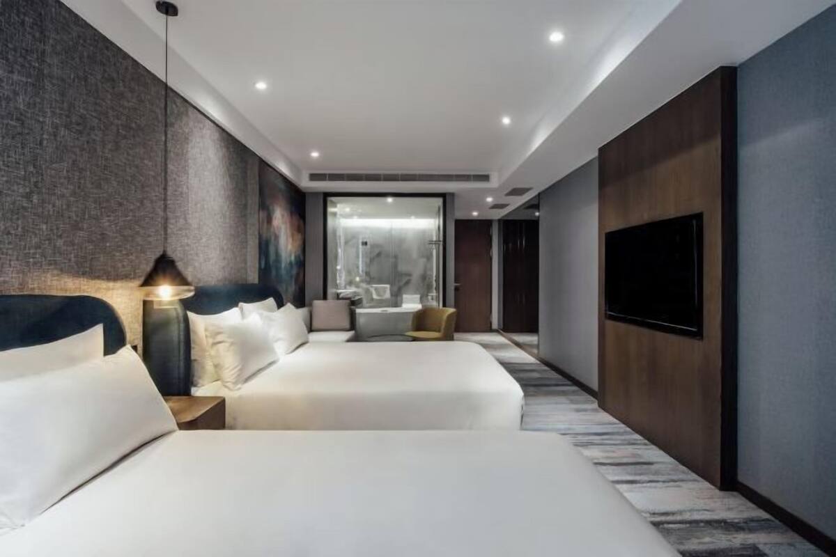 Una habitación de hotel moderna con una cama grande, mesitas de noche, un televisor y un baño con ducha de vidrio.